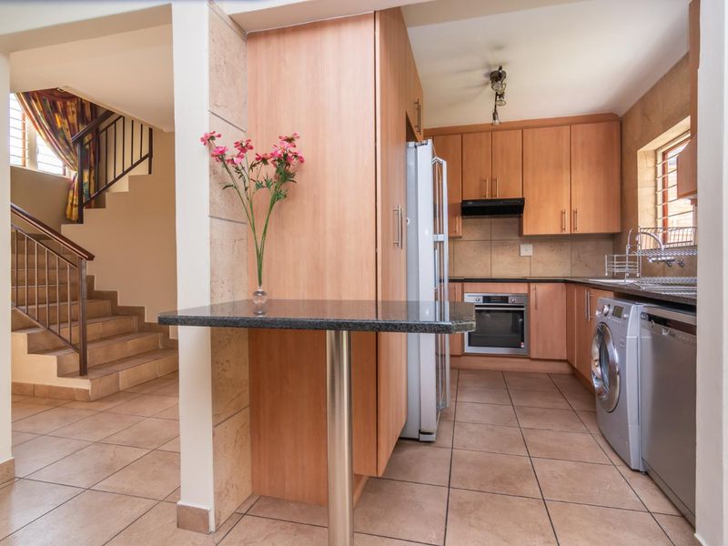 A functional kitchen featuring wood-finish cabinetry, granite countertops, built-in oven, and tiled flooring, adjacent to an internal staircase.