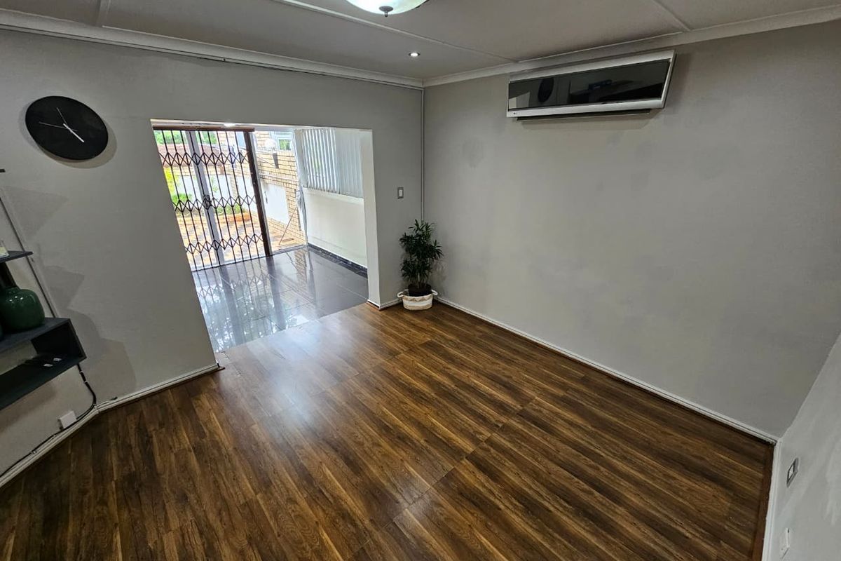 A bright living room featuring wood-look laminate flooring, a wall-mounted air conditioning unit, and direct access to an enclosed patio area.