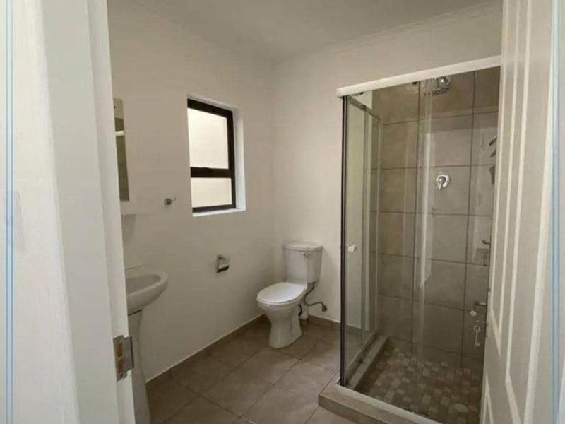 A functional bathroom featuring a glass-enclosed shower, pedestal basin, and toilet with neutral floor tiling.