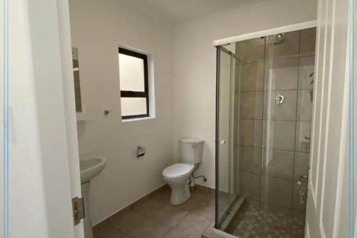 A functional bathroom featuring a glass-enclosed shower, pedestal basin, and toilet with neutral floor tiling.