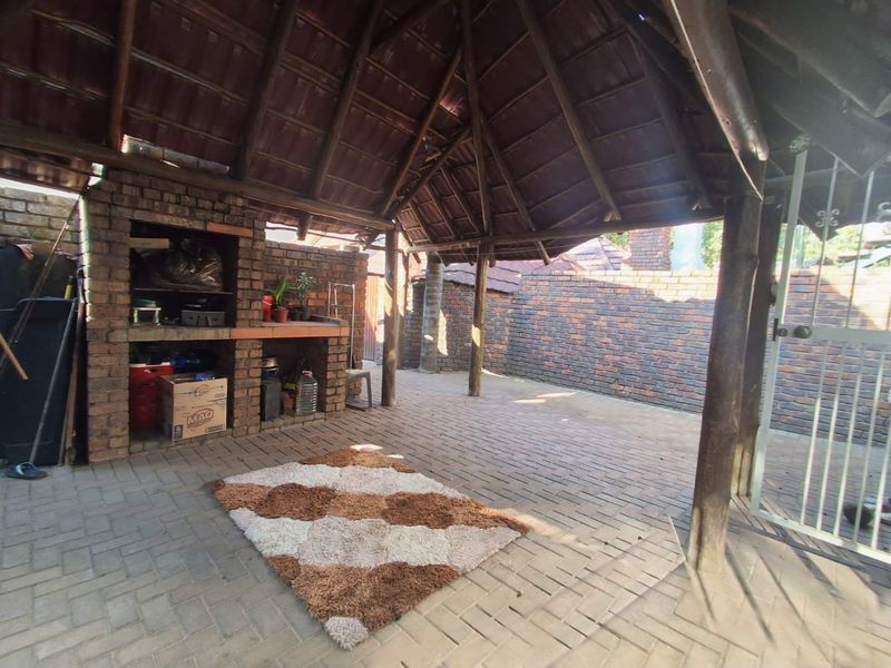 Covered outdoor patio area featuring a built-in brick braai, thatched roof, and paved flooring, ideal for outdoor entertaining.