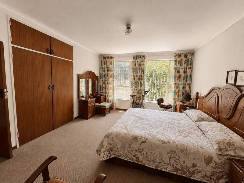 Spacious bedroom featuring built-in wooden cupboards, carpeted flooring, and large windows fitted with security bars.