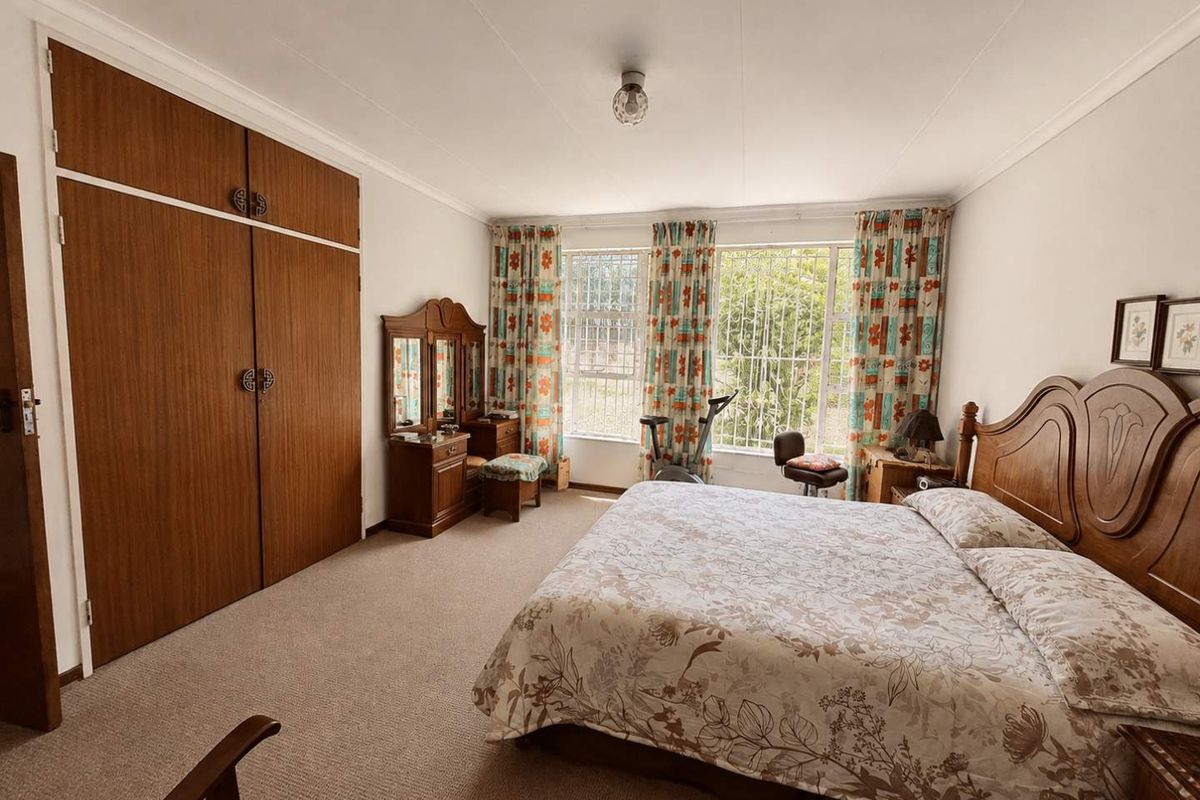 Spacious bedroom featuring built-in wooden cupboards, carpeted flooring, and large windows fitted with security bars.