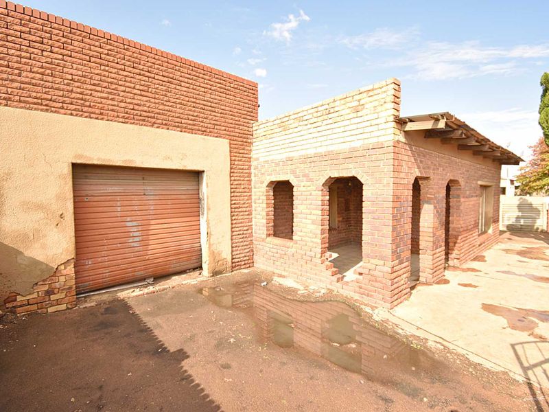 Rear exterior view showing a garage with a roller door and an adjacent brick structure requiring significant maintenance and repair.