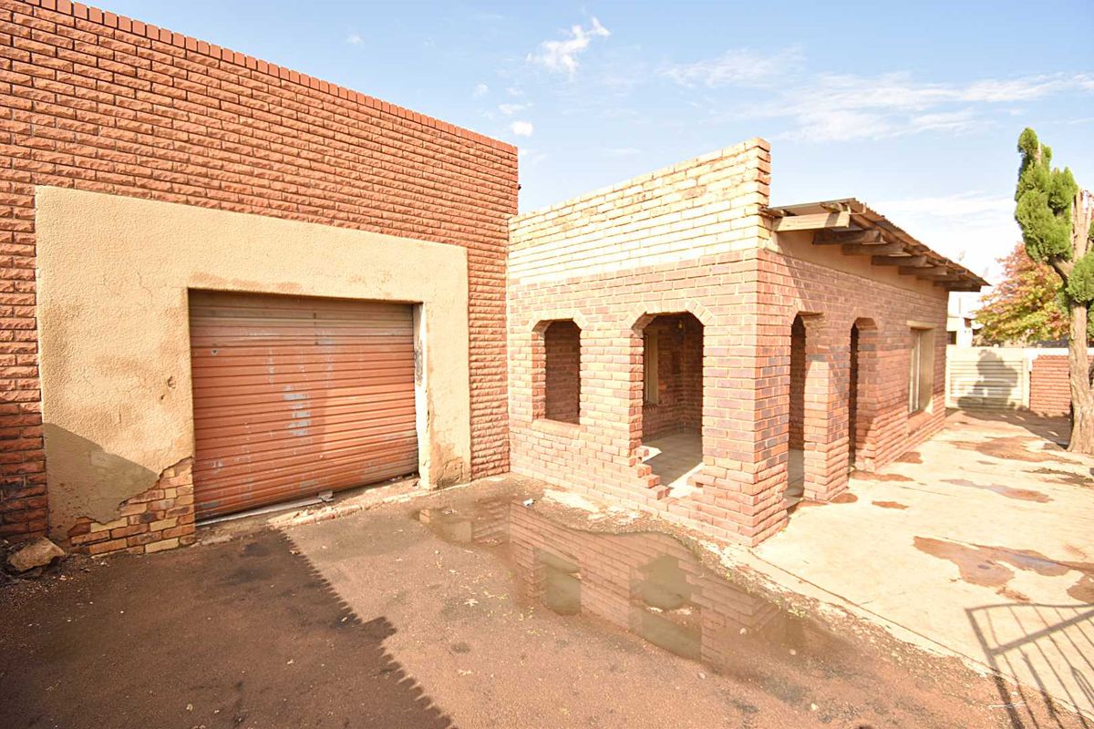 Rear exterior view showing a garage with a roller door and an adjacent brick structure requiring significant maintenance and repair.