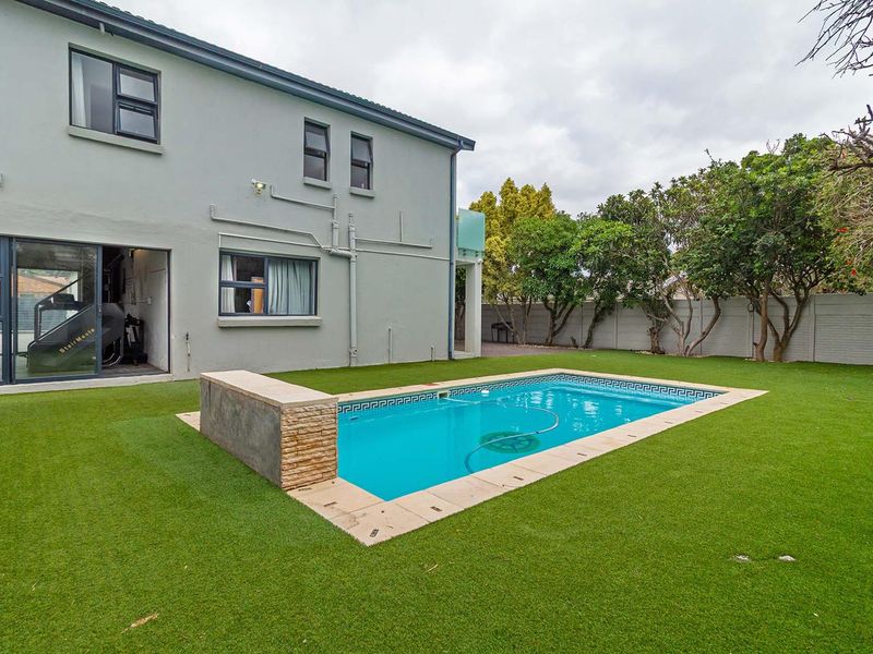A well-maintained rear garden featuring a swimming pool with a stone-clad water feature, surrounded by artificial lawn and a secure boundary wall.