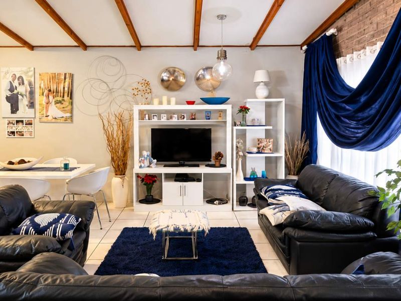 Spacious living area featuring exposed timber ceiling beams, a textured brick feature wall, and neutral tiled flooring.