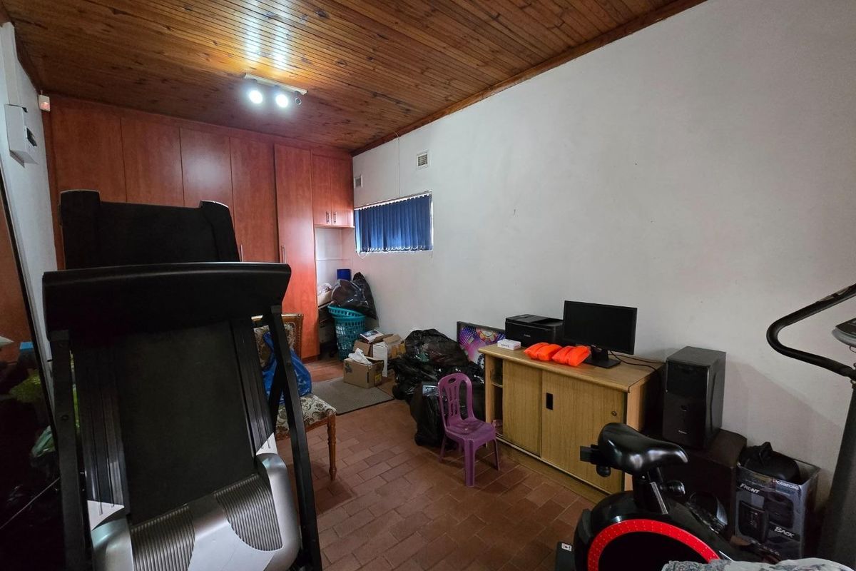 A bedroom featuring built-in cupboards, a timber-clad ceiling, and tiled flooring, currently utilized as a multi-purpose storage and exercise space.