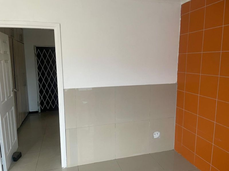 An empty kitchen area featuring tiled walls and flooring, with a doorway leading to an adjacent space secured by a metal gate.