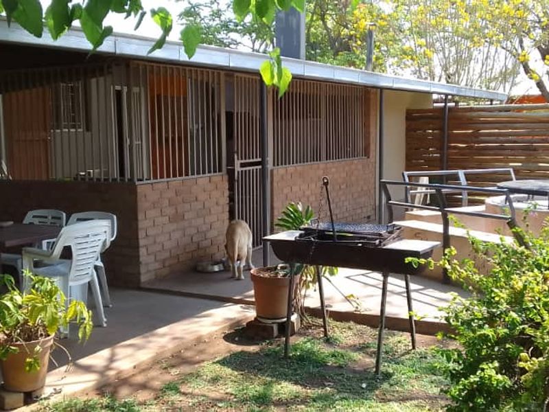 A covered outdoor patio area featuring brick walls, metal security bars, and an adjacent open-air seating space with a built-in fire pit.