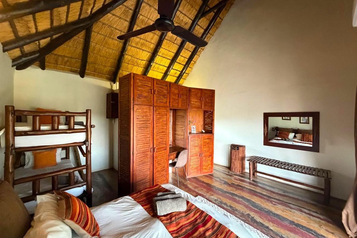 Spacious bedroom featuring a high thatched ceiling with exposed timber rafters, built-in wooden cabinetry, and a ceiling fan.