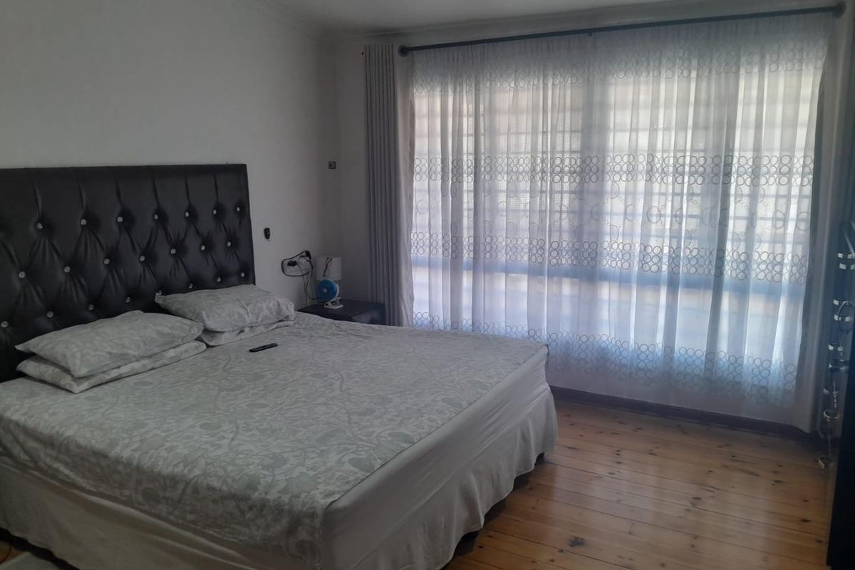 A bedroom featuring timber flooring and large windows with curtain tracks, providing natural light.