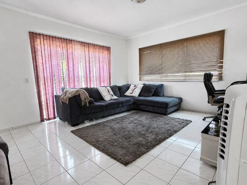 A bright living room featuring white walls, tiled flooring, and large windows with both vertical and venetian blinds for adjustable natural light.