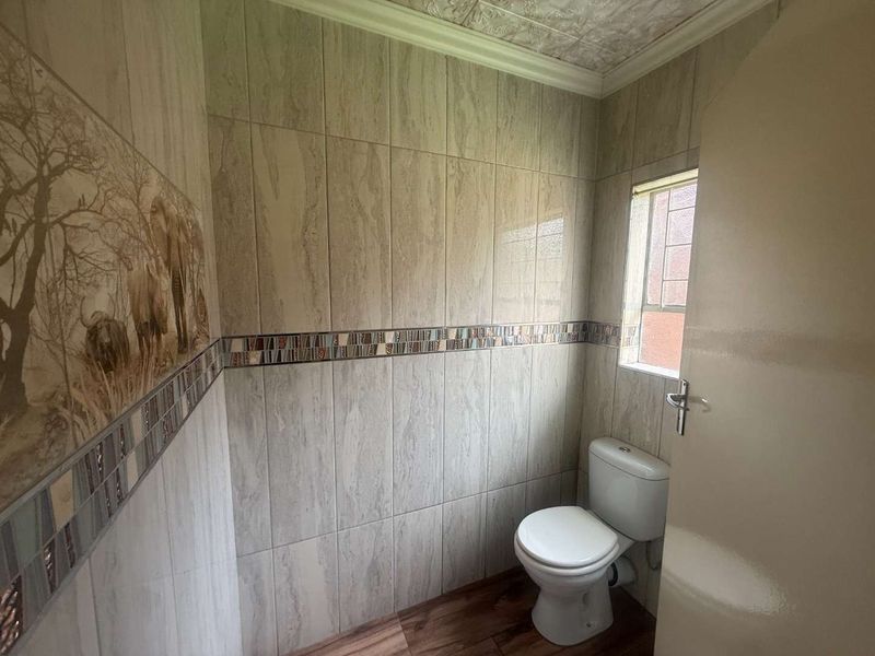 A compact bathroom featuring tiled walls with a decorative border, laminate flooring, and a standard toilet.