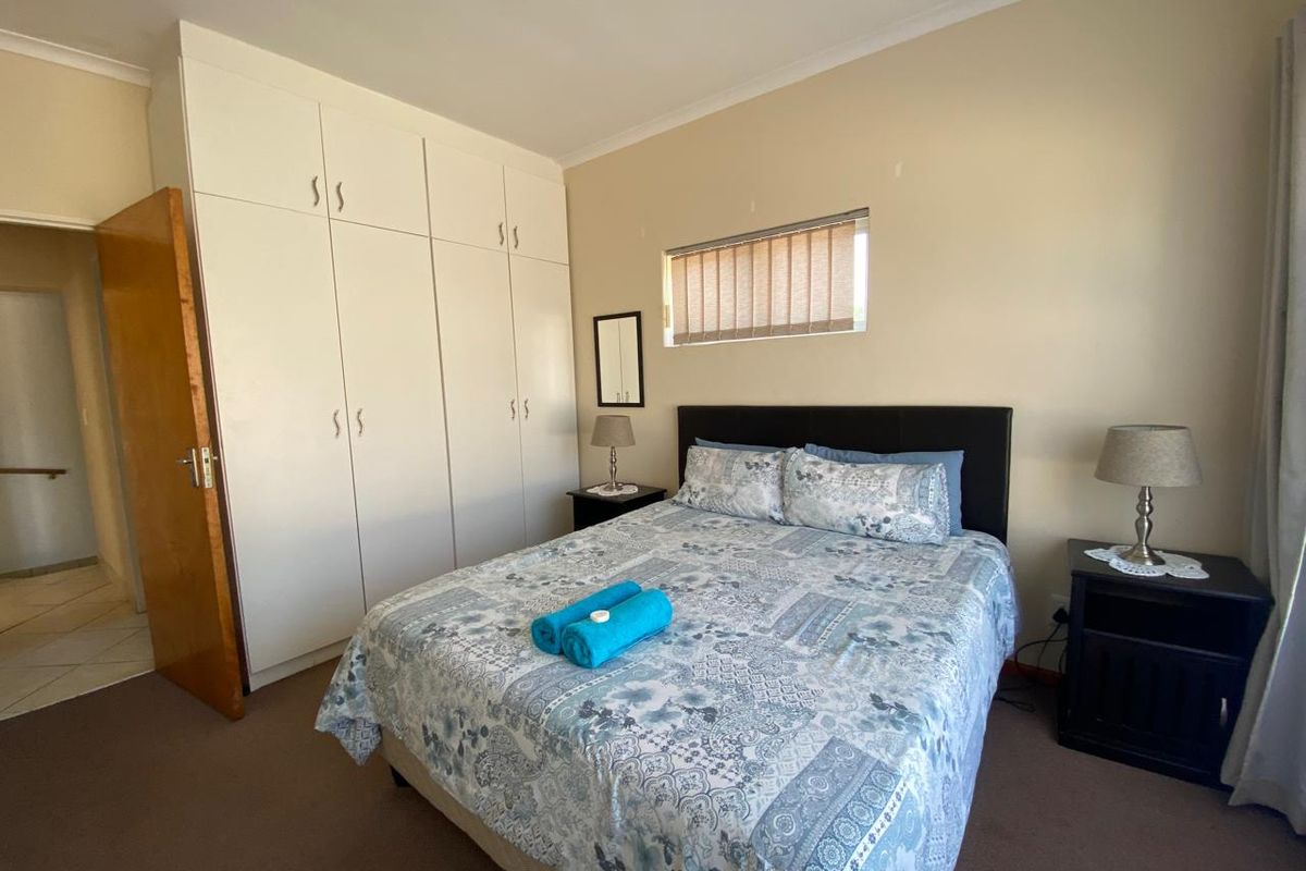 A functional bedroom featuring built-in cupboards, neutral wall finishes, and a high-level window with fitted blinds.