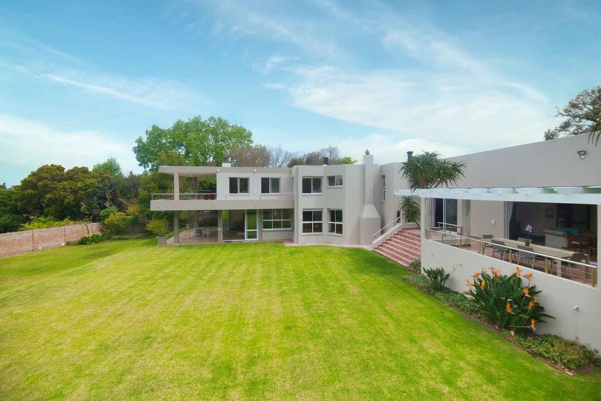 Spacious rear garden view featuring a large lawn, covered patio, balcony, and pergola, showcasing the property's modern architectural design and outdoor living spaces.