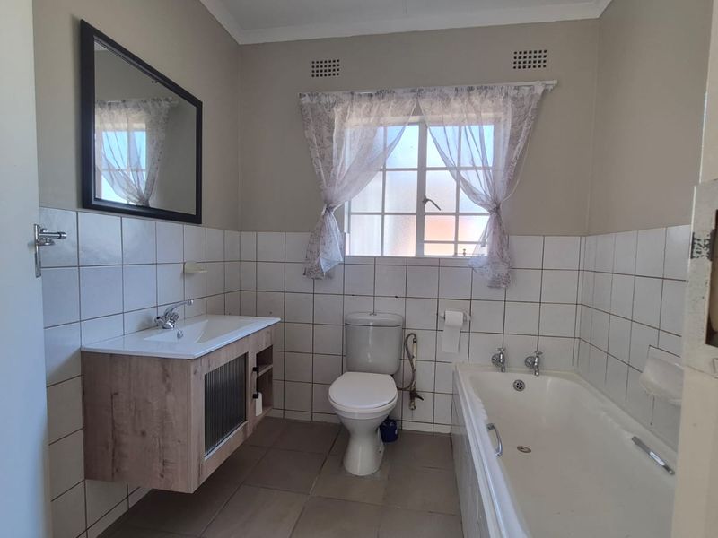 A functional bathroom featuring a modern vanity cabinet, a standard bathtub, a toilet, and tiled finishes throughout.
