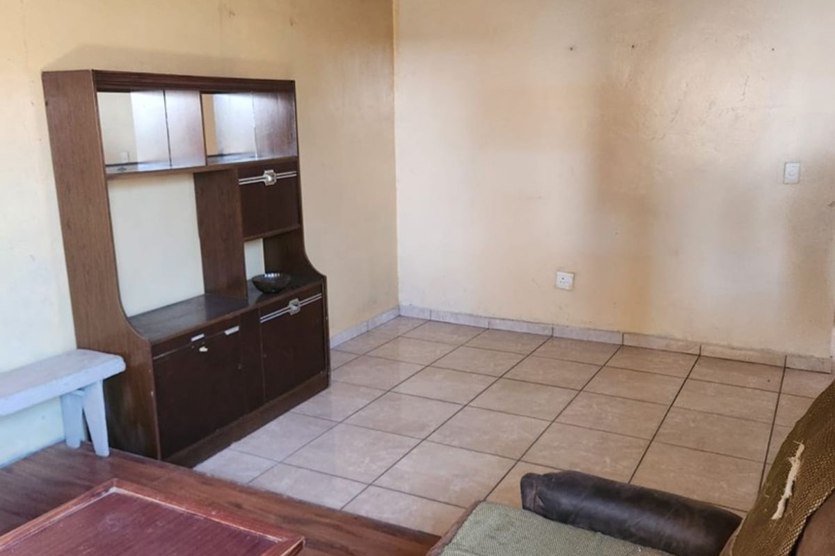 A living room area featuring tiled flooring and textured ceiling tiles, requiring cosmetic updates to improve the overall aesthetic and condition.