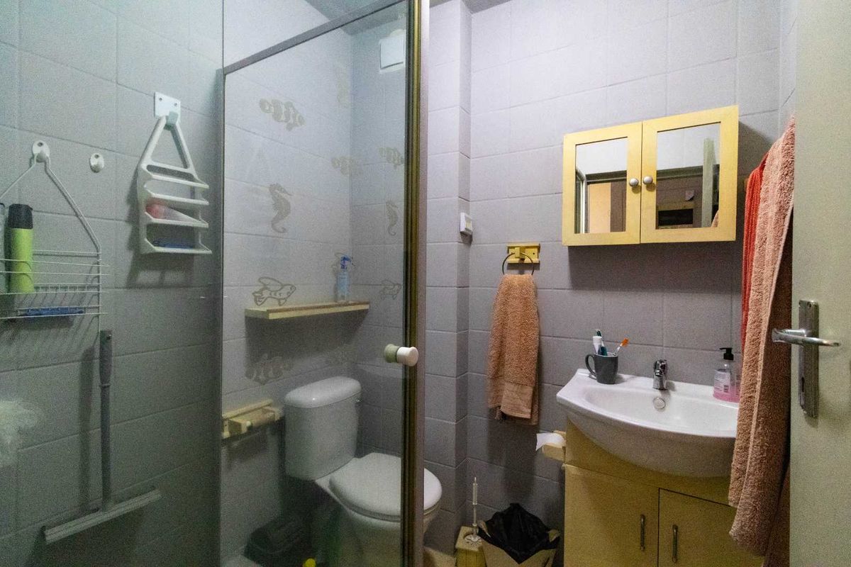 A compact bathroom featuring a shower enclosure, toilet, and vanity unit with a wall-mounted medicine cabinet, finished with neutral wall tiles.