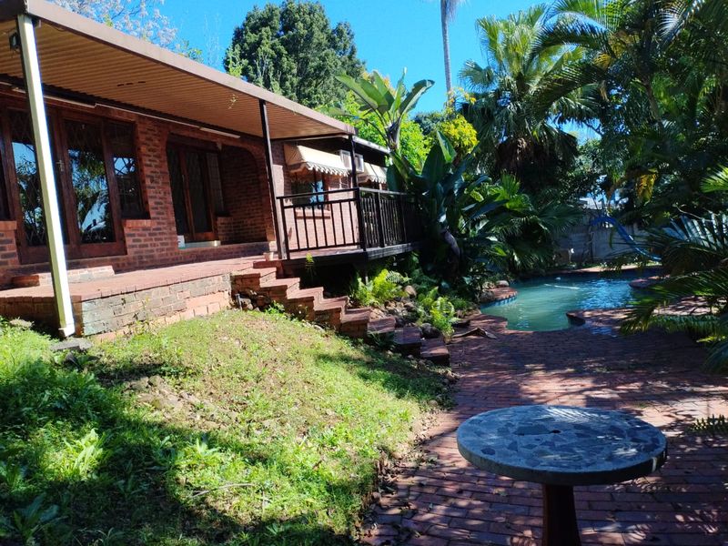 Rear exterior view featuring a brick facade, covered patio area, and a swimming pool set within a landscaped garden.