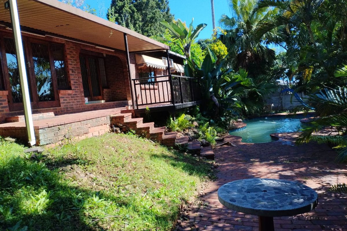 Rear exterior view featuring a brick facade, covered patio area, and a swimming pool set within a landscaped garden.