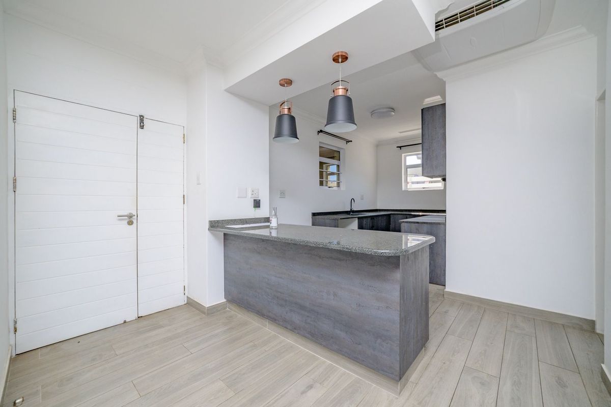 Modern kitchen featuring dark grey cabinetry, granite countertops, a breakfast bar, and neutral laminate flooring in a clean, open-plan layout.