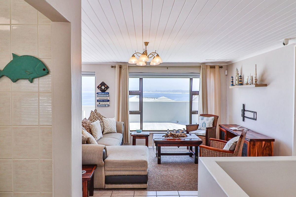 A bright living room featuring a tongue-and-groove ceiling, large windows with ocean views, and direct access to an outdoor balcony area.