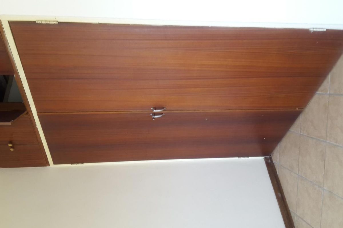 A bedroom featuring built-in wooden cupboards and tiled flooring, presenting a dated aesthetic in need of modernization.