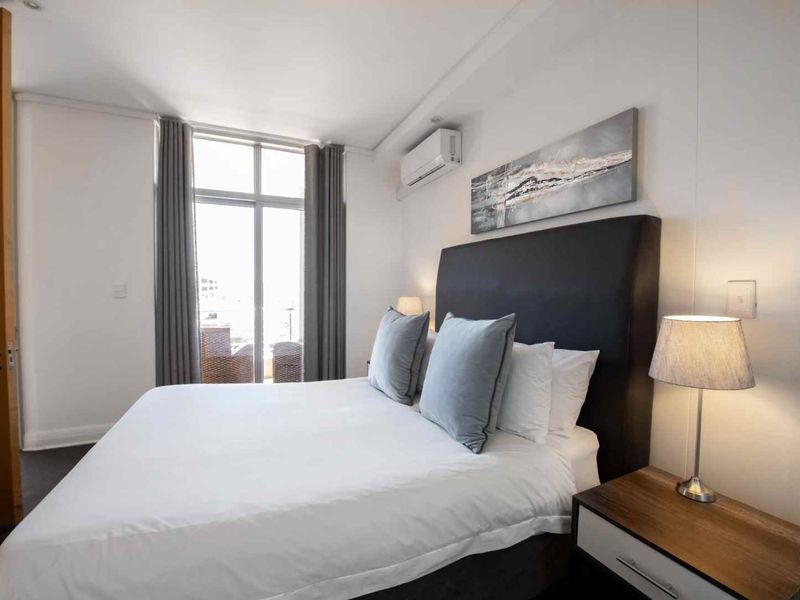 A well-maintained bedroom featuring a split-system air conditioner, neutral finishes, and a sliding glass door providing access to an outdoor balcony area.