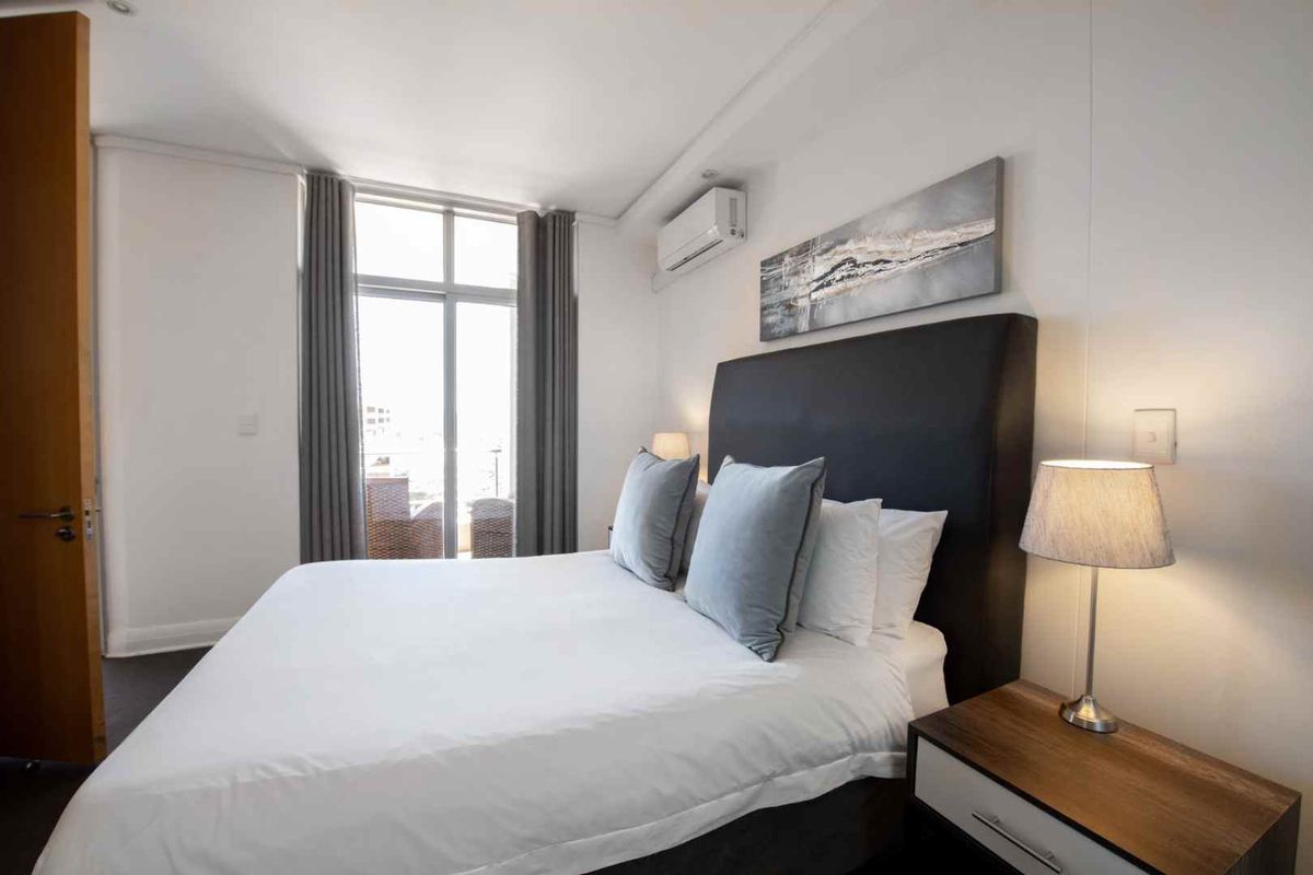 A well-maintained bedroom featuring a split-system air conditioner, neutral finishes, and a sliding glass door providing access to an outdoor balcony area.