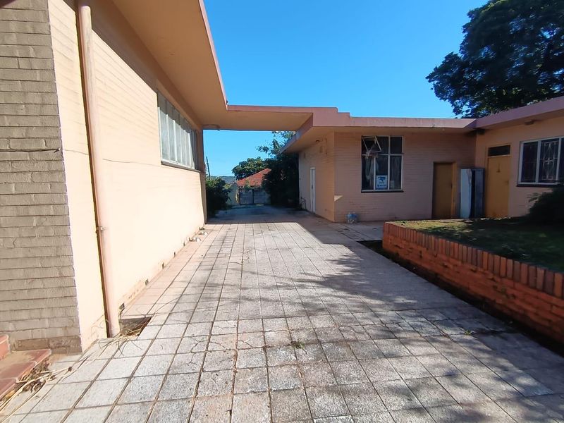 Rear exterior view showing a paved courtyard area, brick retaining wall, and covered walkway connecting building sections.