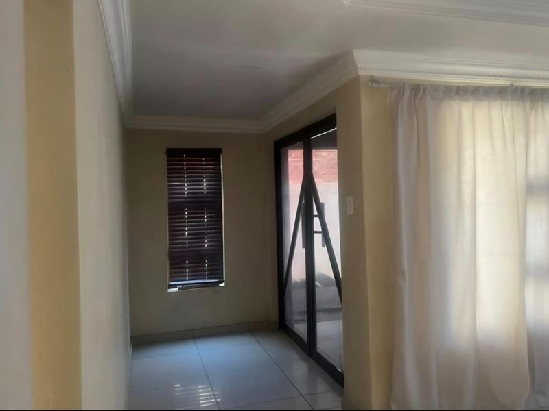An empty living area featuring tiled flooring, decorative cornicing, and a sliding glass door providing access to the exterior.