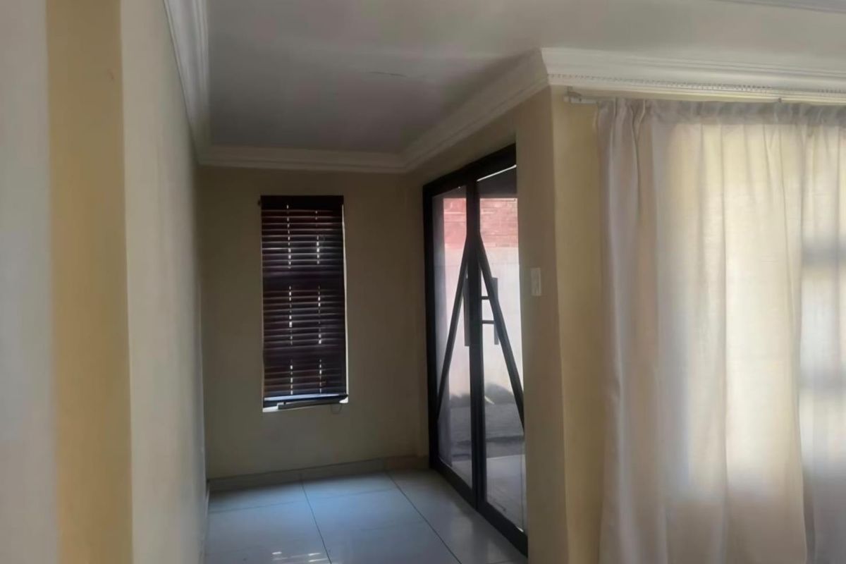 An empty living area featuring tiled flooring, decorative cornicing, and a sliding glass door providing access to the exterior.