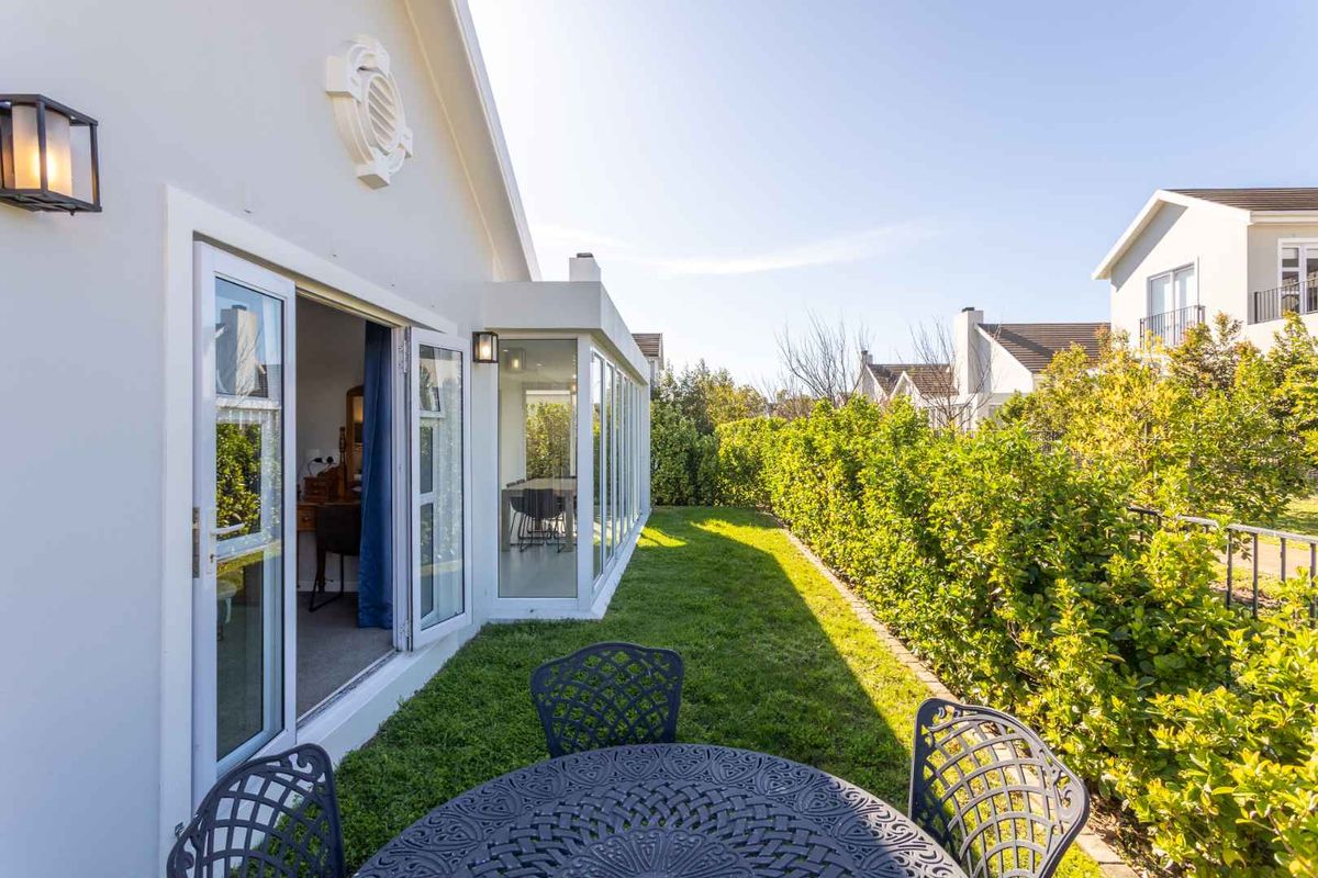 A well-maintained rear garden featuring a manicured lawn, established hedge privacy screening, and direct access to the interior via glass sliding doors.