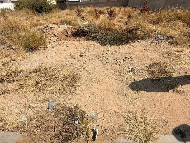 A vacant residential plot featuring dry, overgrown vegetation and uneven terrain, ready for development.