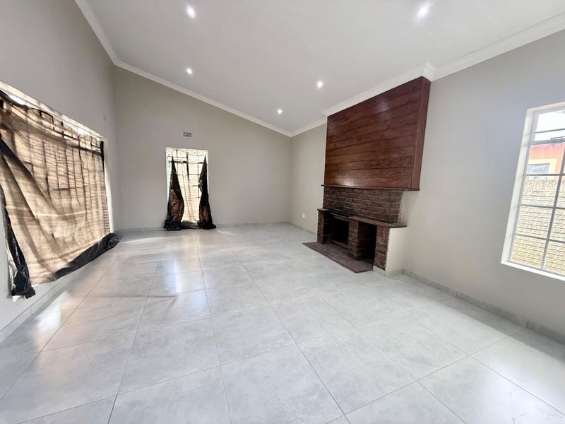 Spacious living room featuring a vaulted ceiling, tiled flooring, recessed lighting, and a prominent brick fireplace with a timber feature wall.