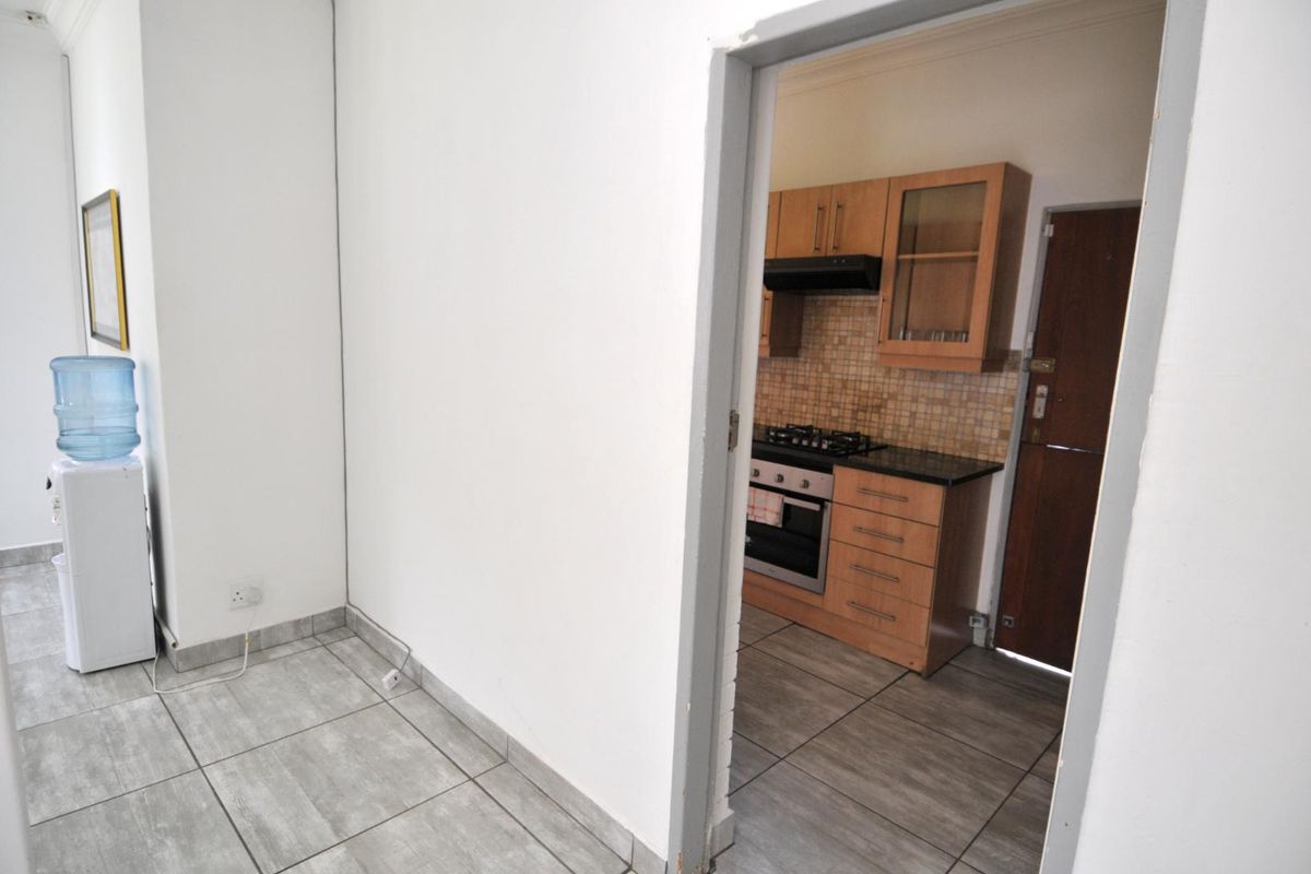 A functional kitchen featuring wooden cabinetry, a gas hob, built-in oven, extractor fan, and tiled flooring, viewed from an adjacent tiled area.