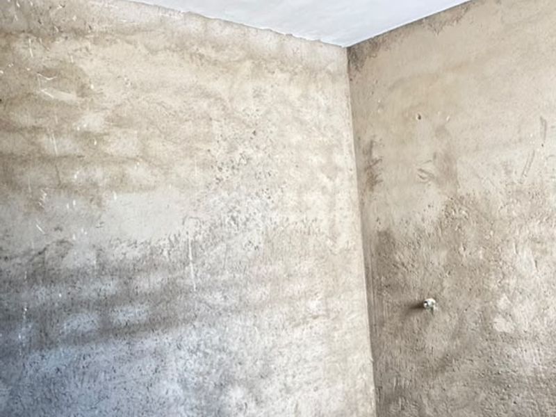 An unfinished bathroom space featuring exposed concrete walls, a prepared shower base, and plumbing rough-ins, ready for final tiling and fixture installation.