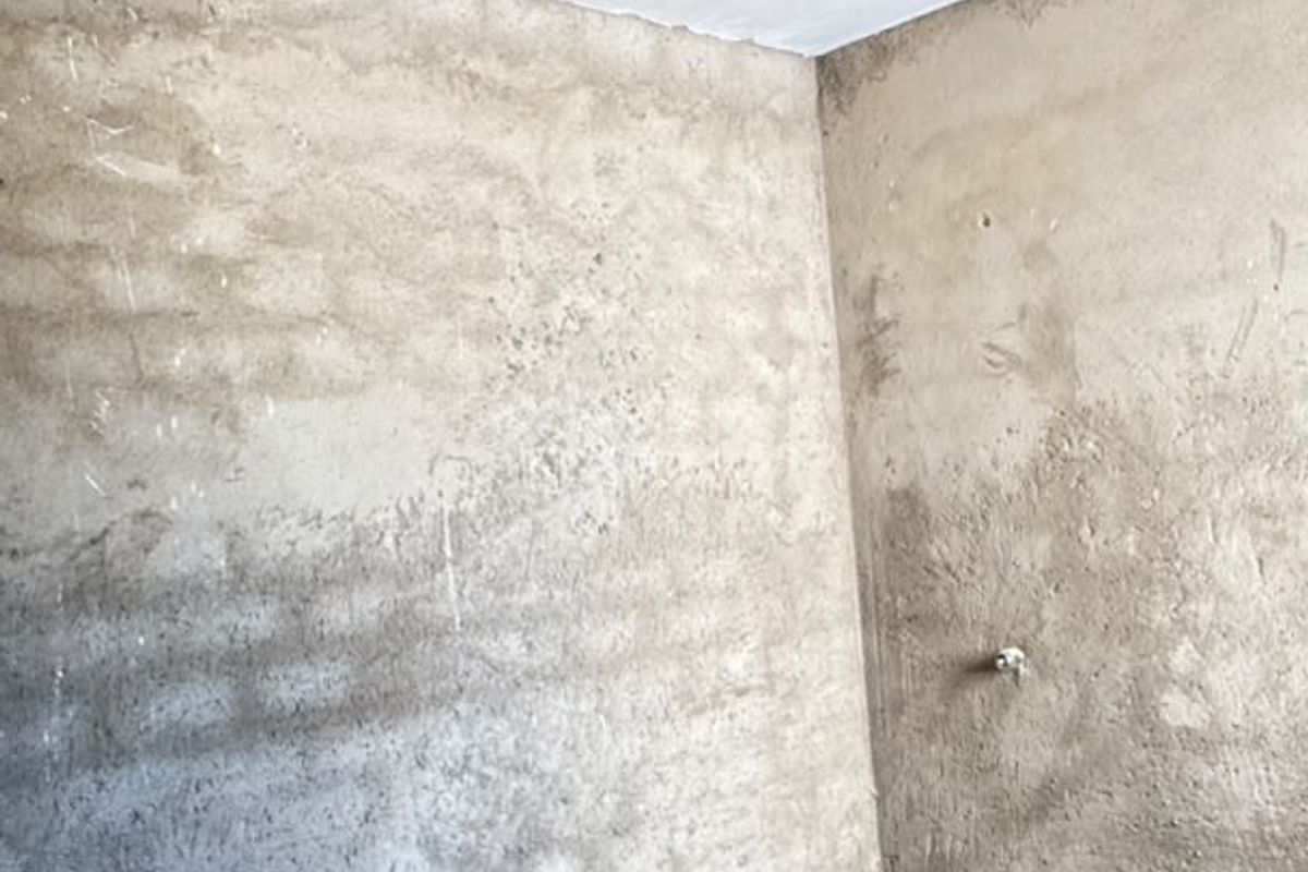 An unfinished bathroom space featuring exposed concrete walls, a prepared shower base, and plumbing rough-ins, ready for final tiling and fixture installation.