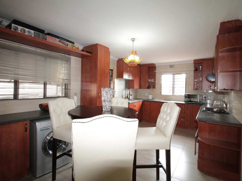 A functional kitchen featuring wood-finish cabinetry, dark countertops, integrated appliances, and tiled flooring, offering a practical layout for daily cooking and dining.