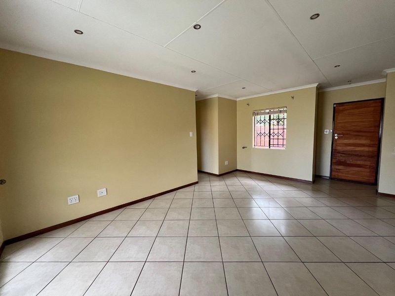 A spacious, empty living area featuring neutral wall tones, tiled flooring, recessed lighting, and a secure window with a metal gate.