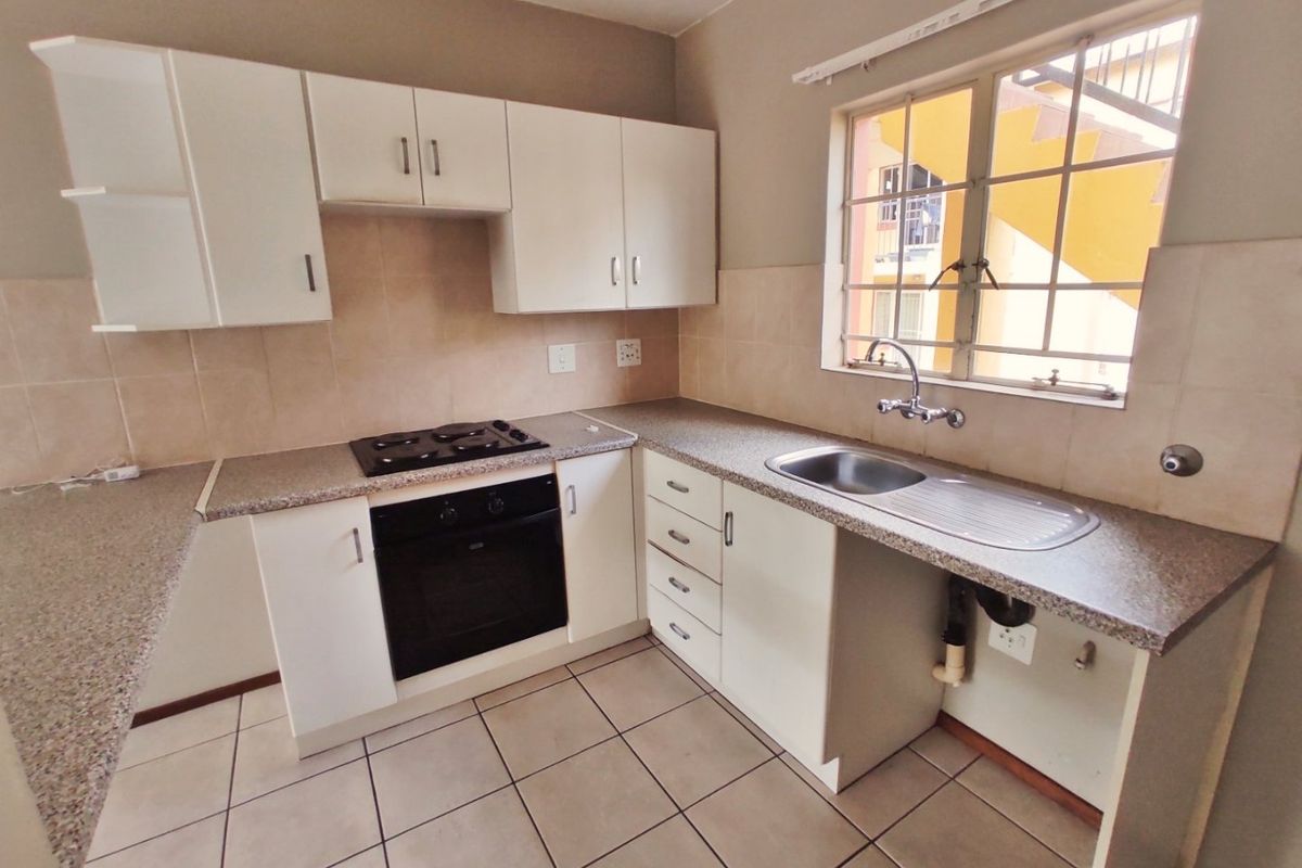 A functional kitchen featuring white built-in cabinetry, laminate countertops, a built-in oven and hob, and tiled flooring with a window for natural light.
