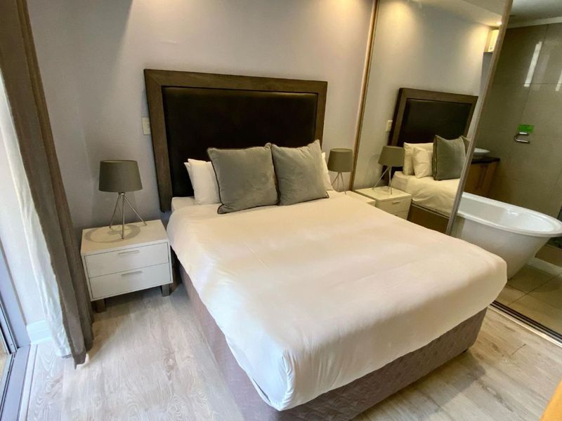 A well-maintained bedroom featuring light-toned laminate flooring and large mirrored sliding wardrobe doors that enhance the sense of space.