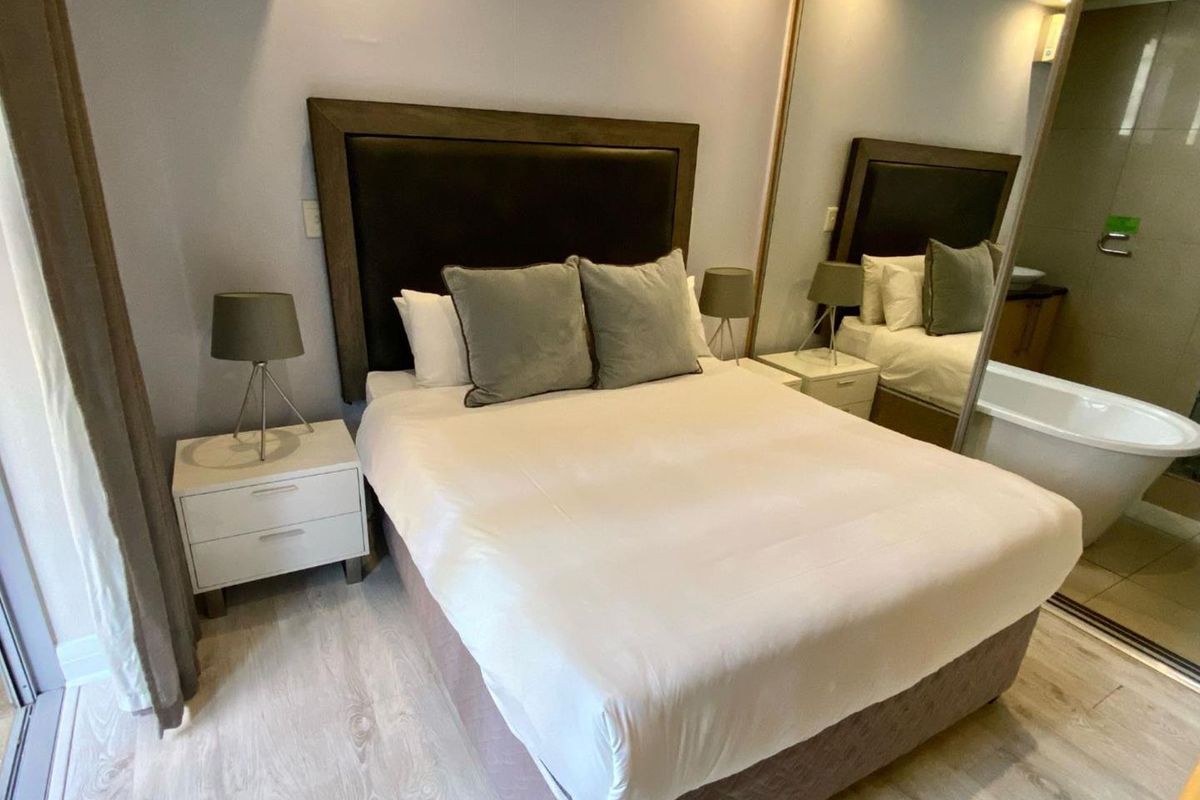 A well-maintained bedroom featuring light-toned laminate flooring and large mirrored sliding wardrobe doors that enhance the sense of space.