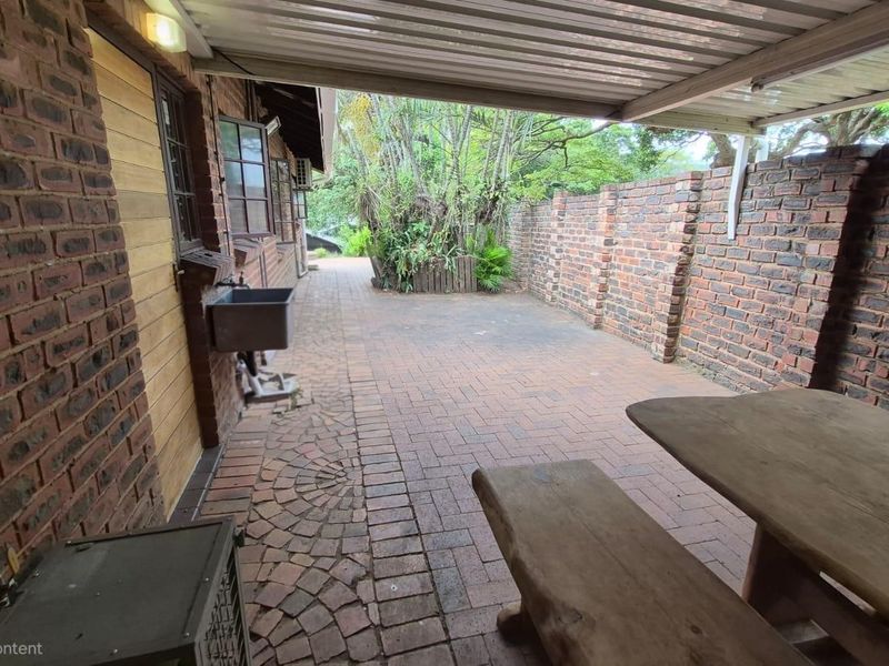A covered outdoor patio area featuring brick paving, a brick boundary wall, and a utility sink, providing a functional space for outdoor living.
