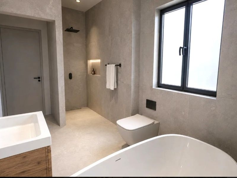 Modern bathroom featuring a walk-in shower, freestanding bathtub, wall-hung toilet, and a vanity with integrated basin, finished with contemporary neutral tiling.