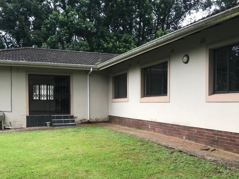 Rear exterior view of the townhouse featuring a lawn, brick plinth detailing, security gates, and tiled roof structure.