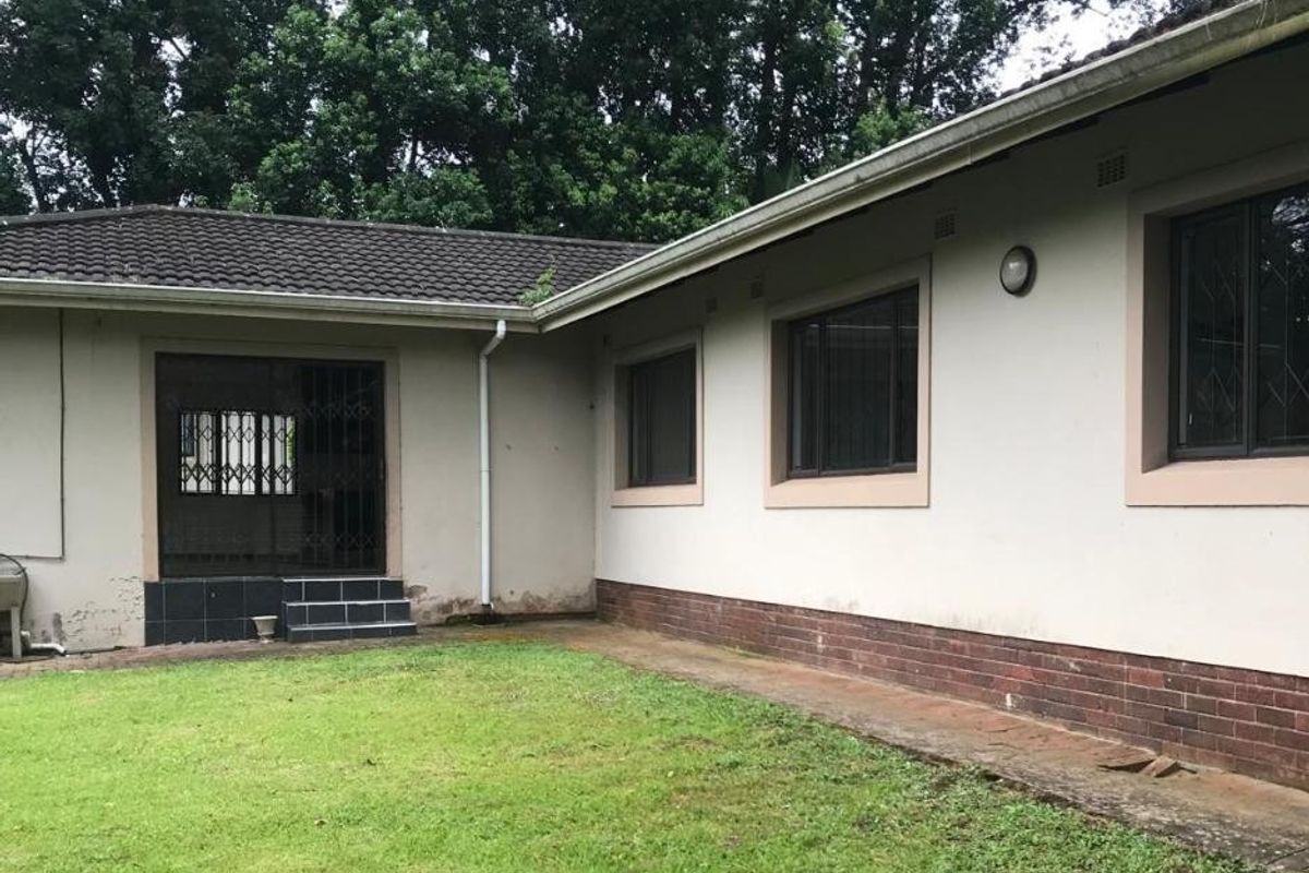 Rear exterior view of the townhouse featuring a lawn, brick plinth detailing, security gates, and tiled roof structure.