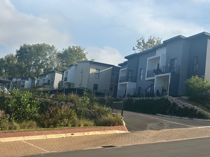 A view of the modern apartment complex exterior featuring paved driveways, landscaped garden areas, and private balconies.