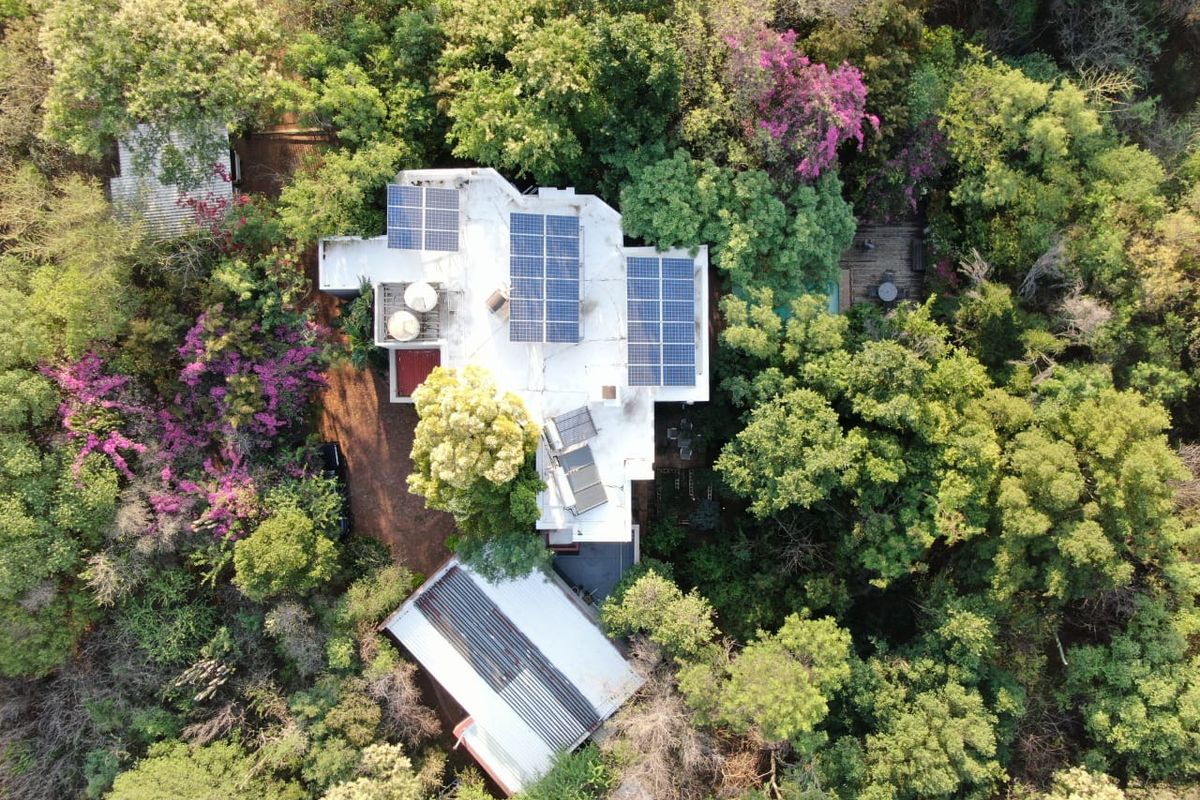 Aerial view of a property nestled in lush greenery, featuring solar panels, water storage tanks, and a solar water heating system on the roof.